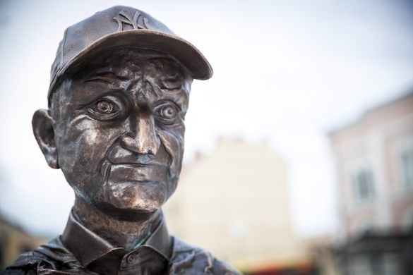 A close up of a bronze statue's wrinkled face wearing a baseball cap