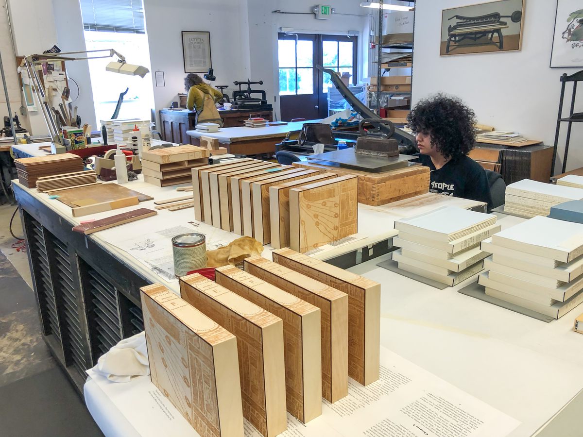 In the bindery, laser-engraved boxes stand ready to hold deluxe editions of <em>Frankenstein</em>, the latest title published by Arion Press. Lead bookbinder Megan Gibes glues the book block into its hard covers while apprentice Samantha Companatico applies glue to the spine of a block.