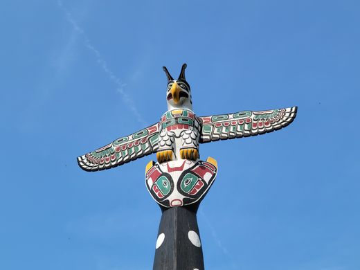 a wood-carved, painted thunderbird sits on a pole in front of a blue sky