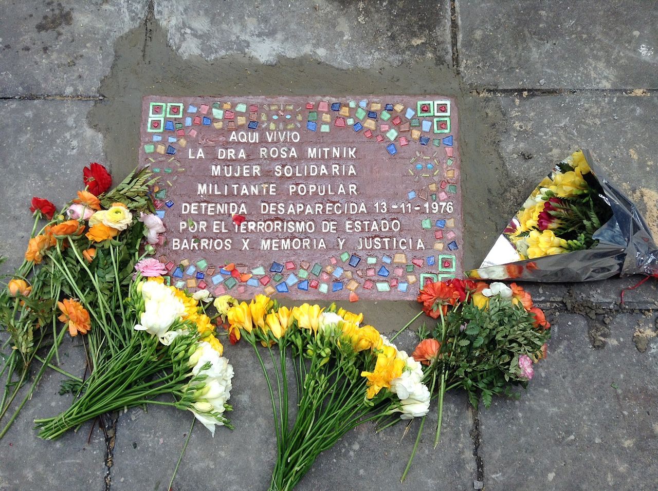 A memorial tile for Rosa Mitnik, surrounded by flowers.