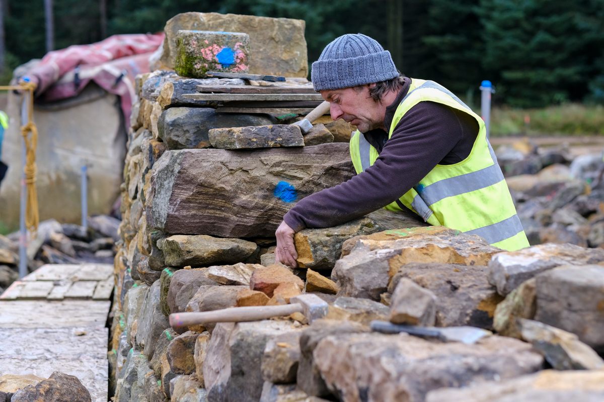 A waller carefully stacks sandstone to produce sturdy walls without the use of mortar.