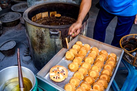 A baker at Kanoom Farung Lan Mea Pao picks freshly baked cakes out of the charcoal brazier and moves them to a metal box to cool.