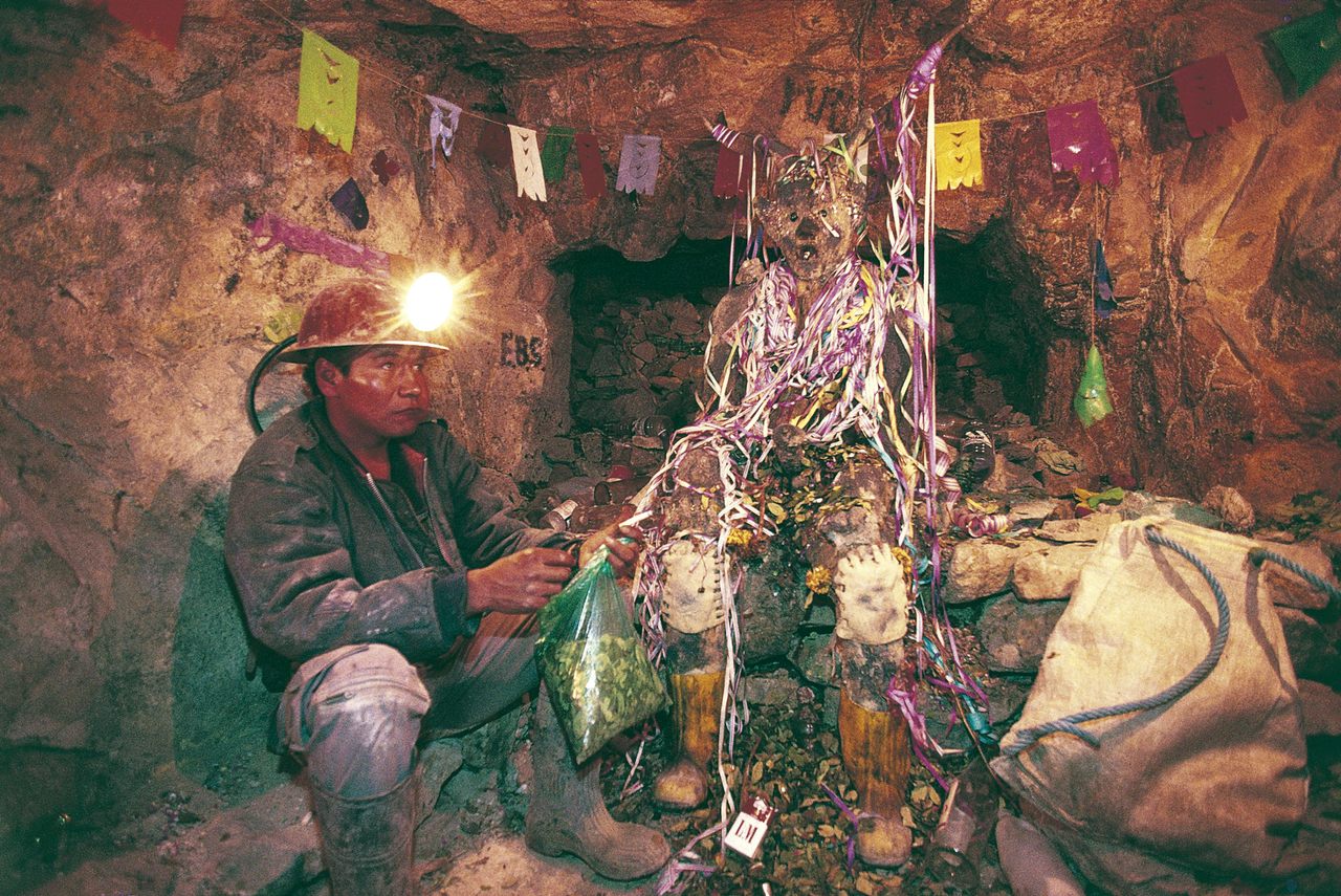 A miner sits at the feet of El Tio, leaving offerings for safety and prosperity.