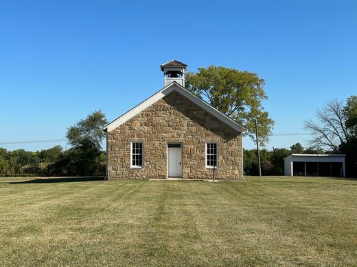 the front of a small, one-room limestone schoolhouse with two windows, one door, and gabled roof.