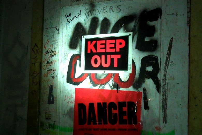A graffiti-covered door in a dark space features a Keep Out sign and a red Danger sign.