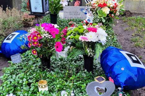 Fan memorabilia on grave, including unopened beer.