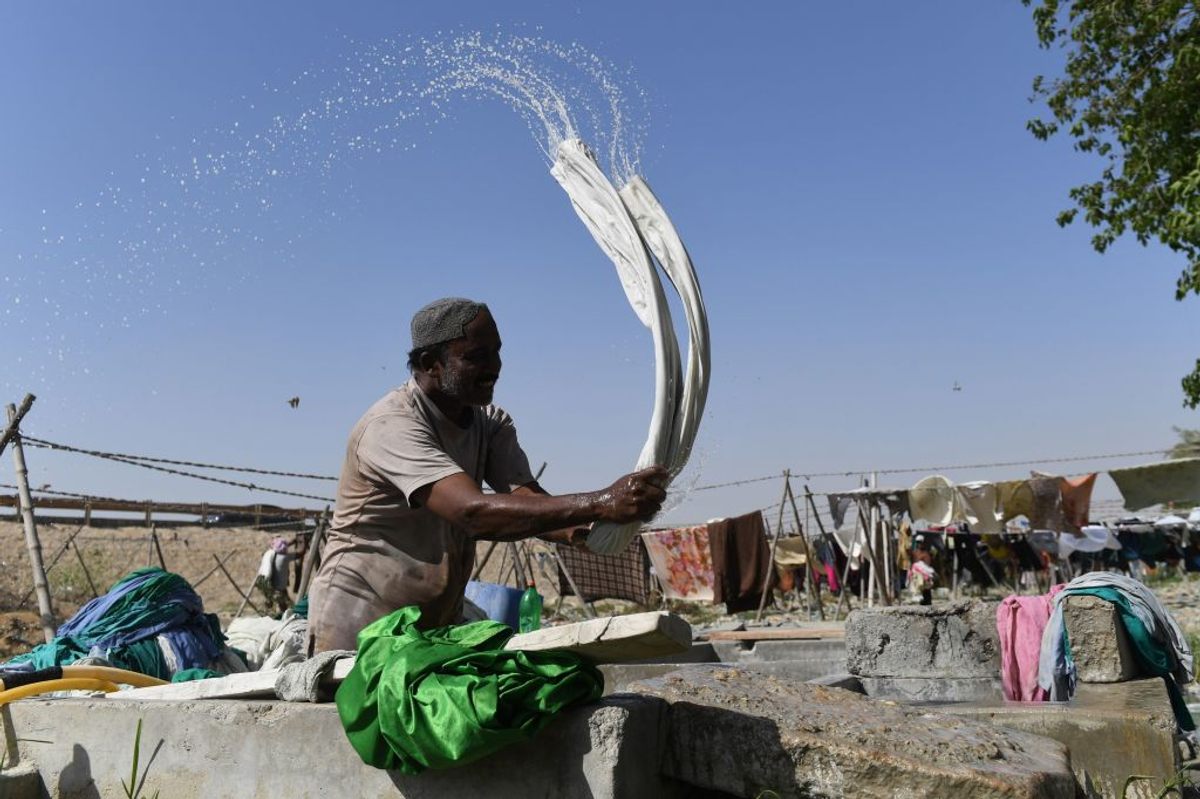 A dhobi beats wet clothes on a stone as part of the washing process.