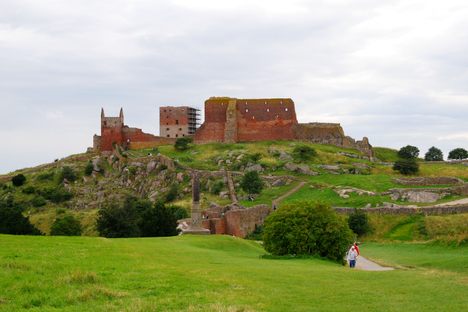 Red-stone castle ruins sit atop a green hill