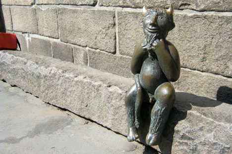 The devil sits on the stone slab, smiling at passers-by