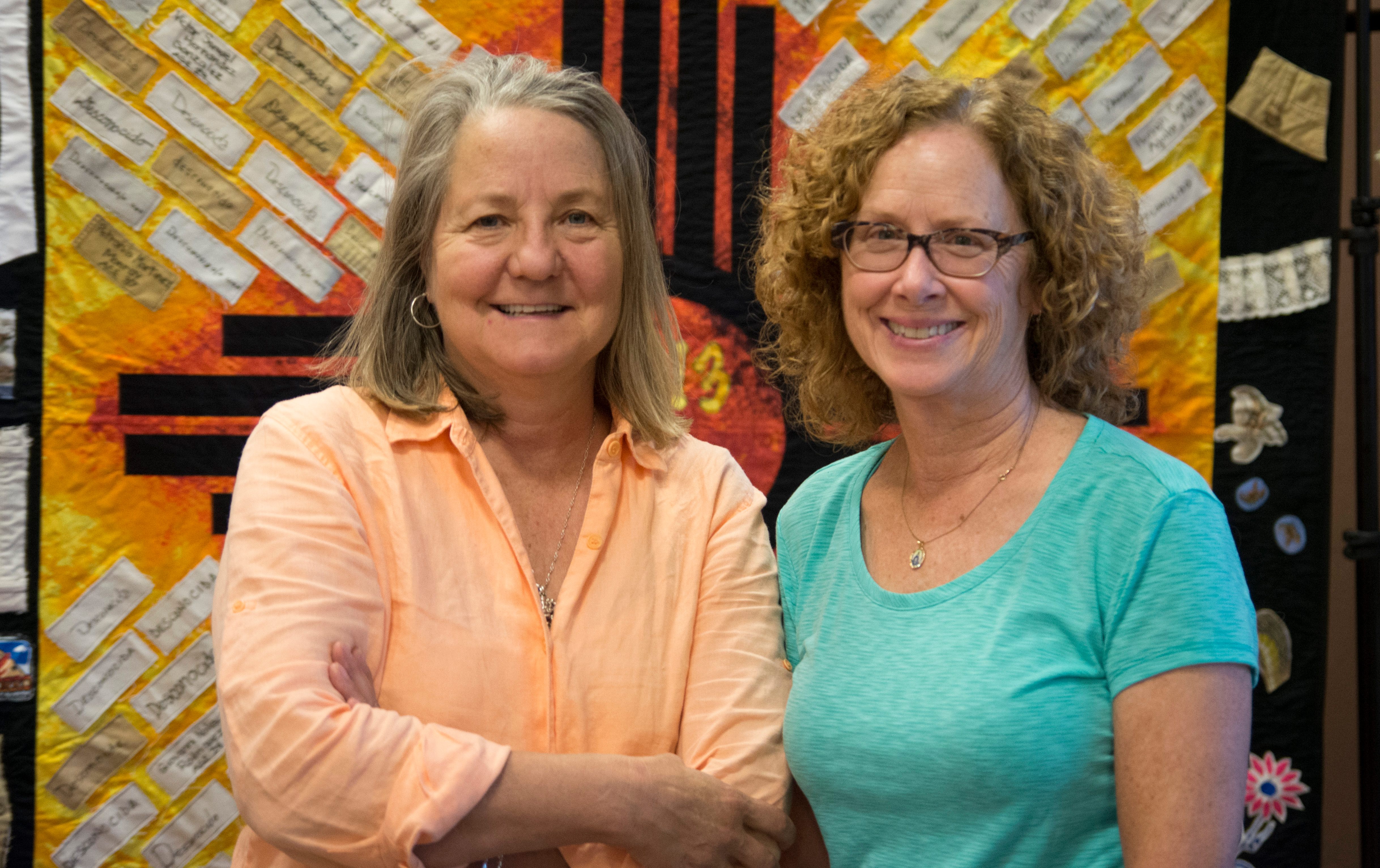 Jody Ipsen, left, and Peggy Hazard, right, stand in front of a quilt from the Migrant Quilt Project.