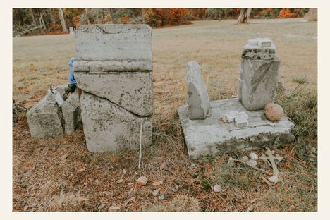 Broken and leaning headstones at Pere Cheney Cemetery surrounded by pine needles and offerings left by visitors to honor the forgotten dead.