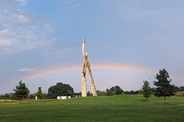 A large sculpture in a field with a rainbow behind it.